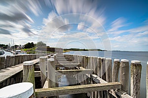 Dynamic moving white clouds against a blue sky above a wooden seahorse near a lake