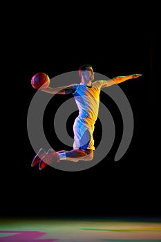 Dynamic photo of doing athlete man, basketball player doing perfect slam dunk in action against black studio background