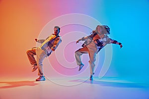 Dynamic photo of two dancers, man and woman move synchronously in hip-hop style dance against gradient background in