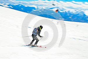 Dynamic picture of a skier on the piste in Alps. Woman skier in the soft snow. Active winter holidays, skiing downhill in sunny