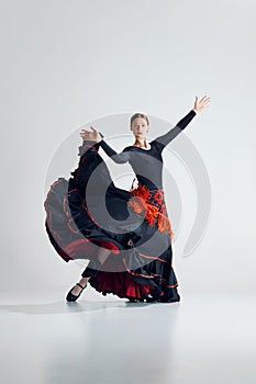 Dynamic portrait of female dancer, elegant woman performing with passion, dancing flamenco against grey studio