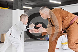 Dynamic portrait of man, professional judo, jiu-jitsu coach training with little boy, child in white kimono. Sportive