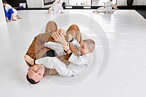Dynamic portrait of man, professional judo, jiu-jitsu coach training with little boy, child in white kimono. Teaching