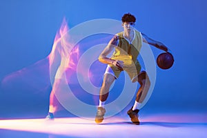 Dynamic portrait of professional basketball player training with ball isolated on blue studio background in mixed neon