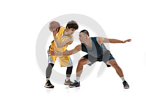 Dynamic portrait of two young basketball players playing basketball isolated on white studio background. Motion