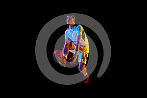 Dynamic portrait of young athlete man training basketball techniques against black studio background in mixed neon light