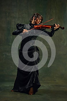 Dynamic pose of passionate female musician, young woman, violinist in black attire, playing violin with intense