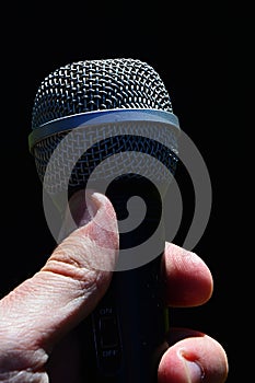 Dynamic professional microphone for vocal and instruments held in man left hand against dark background.