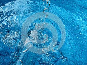 Dynamic splash in crystal clear blue water and glass bottle, creating ripples and water droplets in motion. Clean water