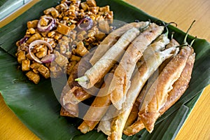 Dynamite lumpia and Tofu in peanut garlic sauce placed on a tray lined with banana leaves. photo