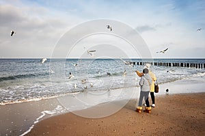 Two women feed birds at the beach on a cold day.