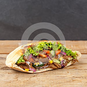 DÃ¶ner Kebab Doner Kebap fast food in flatbread on a wooden board square with copyspace copy space