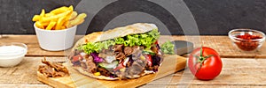 DÃ¶ner Kebab Doner Kebap fast food meal in flatbread with fries on a wooden board panorama