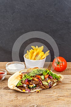 DÃ¶ner Kebab Doner Kebap fast food meal in flatbread with fries on a wooden board portrait format