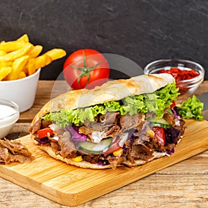 DÃ¶ner Kebab Doner Kebap fast food meal in flatbread with fries on a wooden board square