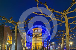 Düsseldorf`s Schlossturm museum with an illuminated ferris wheel surrounded by Platanus trees in the background at night