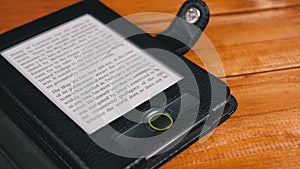 E-book in a case lies on a wooden table. Screen of electronic ink displays text of the book