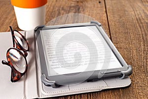 e-book, glasses and cup of coffee on a wooden table. Space for text