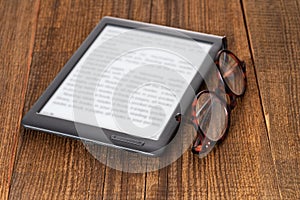 e-book reader and glasses on a wooden table