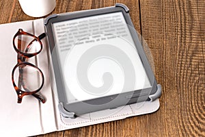 e-book reader and glasses on a wooden table