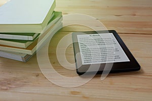 E-book reader and stack of books on wooden