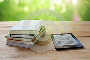 E-book reader and stack of books on wooden table