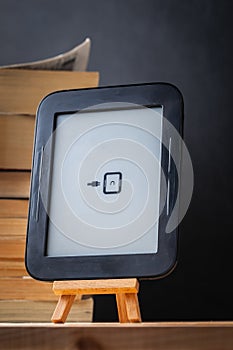 E-book reader on the wooden stand next to the stack of paper books at the black background