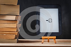 E-book reader on the wooden stand next to the stack of paper books at the black background