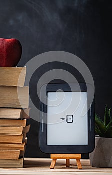 E-book reader on the wooden stand next to the stack of paper books at the black background