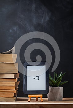 E-book reader on the wooden stand next to the stack of paper books at the black background