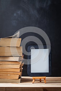E-book reader on the wooden stand next to the stack of paper books at the black background