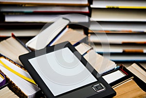 The e-book with a white screen lies on the open multi-colored books that lie on a dark background, close-up