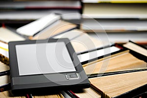 The e-book with a white screen lies on the open multi-colored books that lie on a dark background, close-up