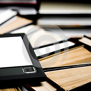 The e-book with a white screen lies on the open multi-colored books that lie on a dark background, close-up