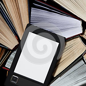 The e-book with a white screen lies on the open multi-colored books that lie on a dark background, close-up