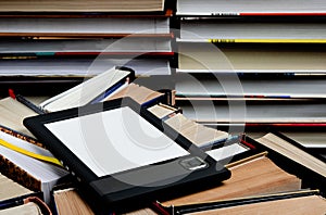 The e-book with a white screen lies on the open multi-colored books that lie on a dark background, close-up