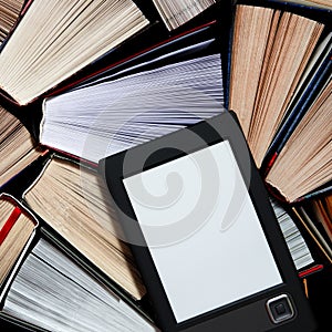 The e-book with a white screen lies on the open multi-colored books that lie on a dark background, close-up