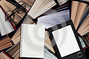 The e-book with a white screen lies on the open multi-colored books that lie on a dark background, close-up