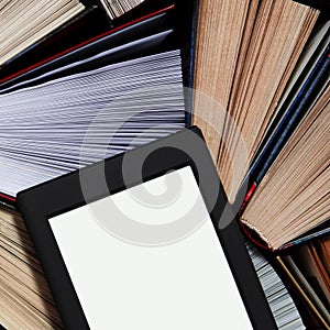 The e-book with a white screen lies on the open multi-colored books that lie on a dark background, close-up