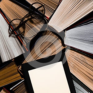 The e-book with a white screen lies on the open multi-colored books that lie on a dark background, close-up