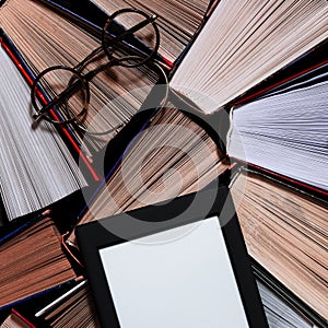 The e-book with a white screen lies on the open multi-colored books that lie on a dark background, close-up