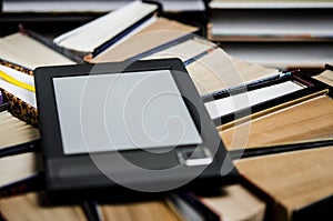 The e-book with a white screen lies on the open multi-colored books that lie on a dark background, close-up