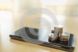 E-Commerce, Business and Technology Concept. Closeup of shopping cart / trolley miniature on stack of coins on mobile smartphone