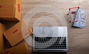 E-commerce concept for top-view photo of laptop, fake US dollar banknote, boxes and trolley