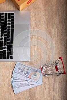 E-commerce concept for top-view photo of laptop, fake US dollar banknote, boxes and trolley