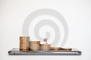 E-Commerce, Money and Financial Concept. Closeup of miniature shopping cart / trolley on stack of coins on mobile smartphone on