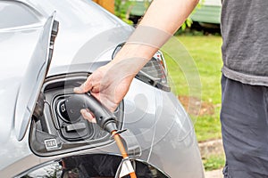 E Electric e-car charge connector close up male person hand and body plugging car into charge