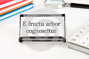 E fructu arbor cognoscitur the phrase in Latin translates as the Tree is known by its fruits on a white business card on a table