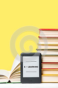 E-learning. E-book reader and a stack of books on a yellow background. Vertical. Copy space. Concept of education and electronic