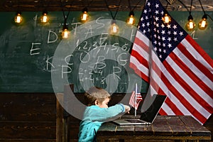 E-learning or online courses at home schooling. Little boy with laptop for business at American flag. Patriotism and